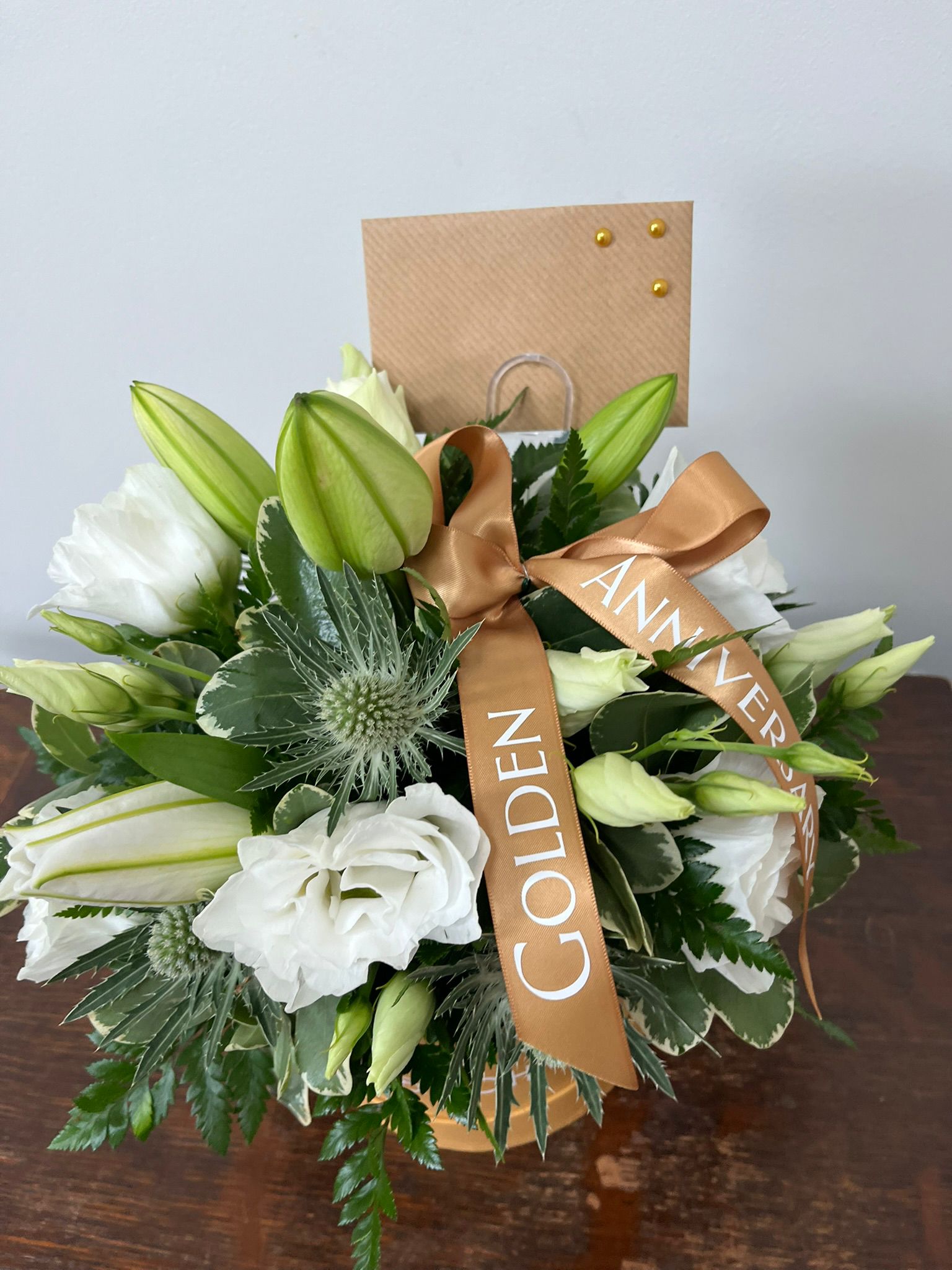 Floral arrangement with a 'Golden Anniversary' ribbon on a wooden surface.