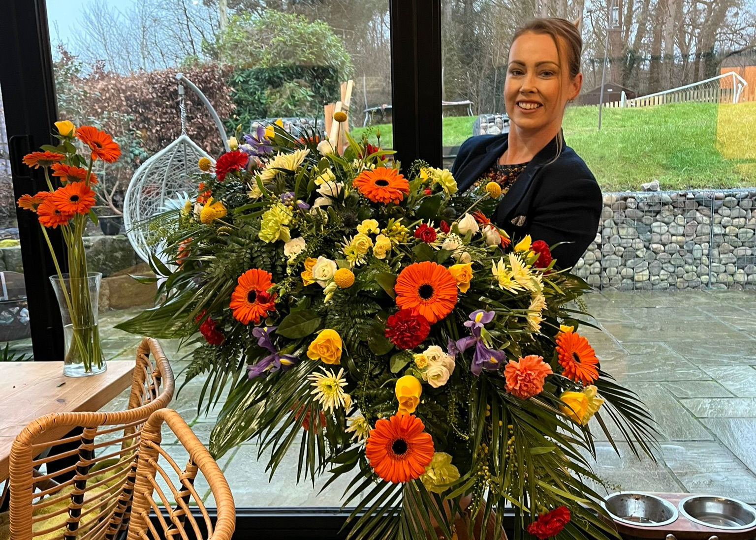 Person holding a large, colorful flower arrangement indoors.