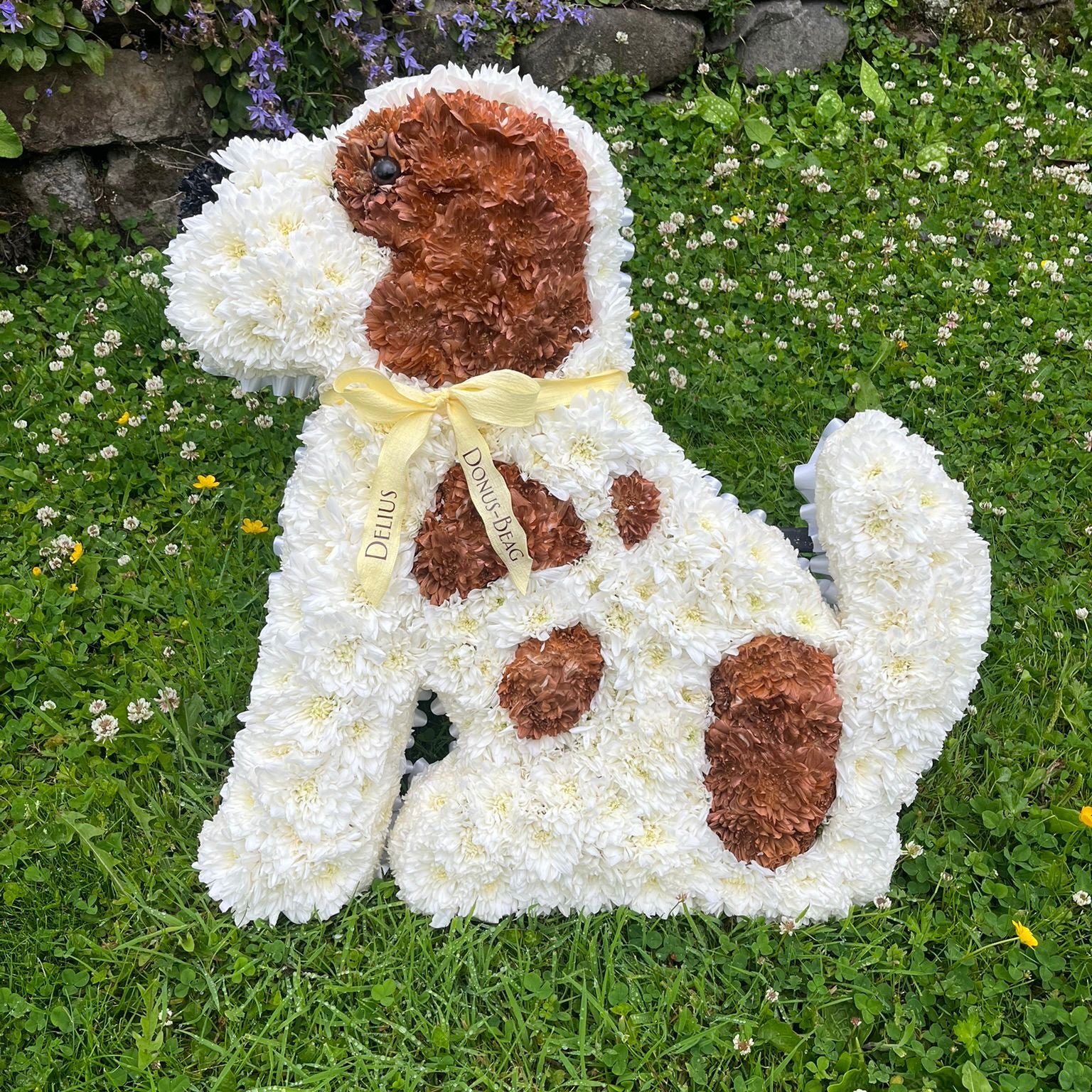 Floral arrangement shaped like a dog with a yellow bow on a grassy background