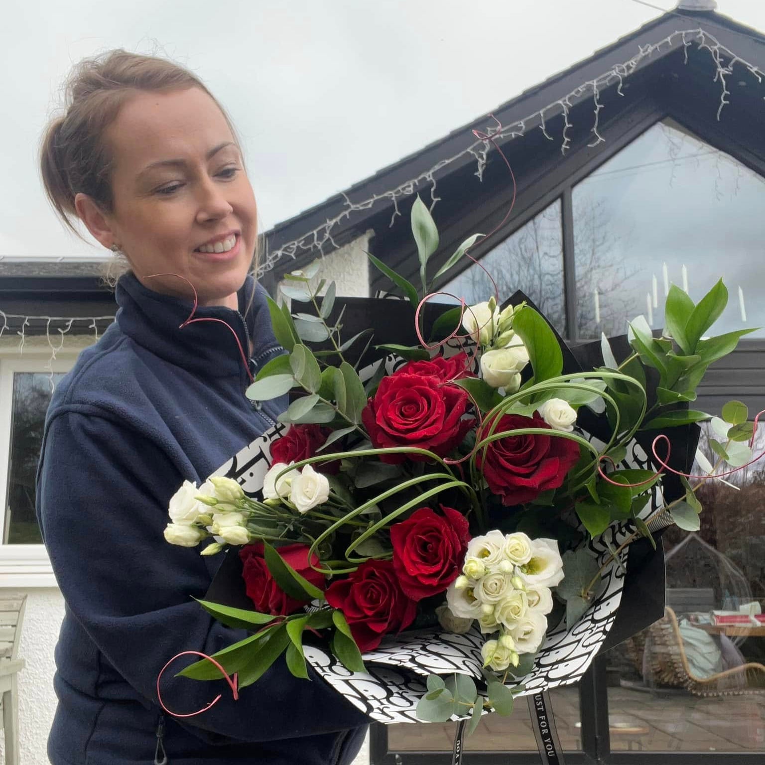 Person holding a large bouquet of red and white flowers outdoors.