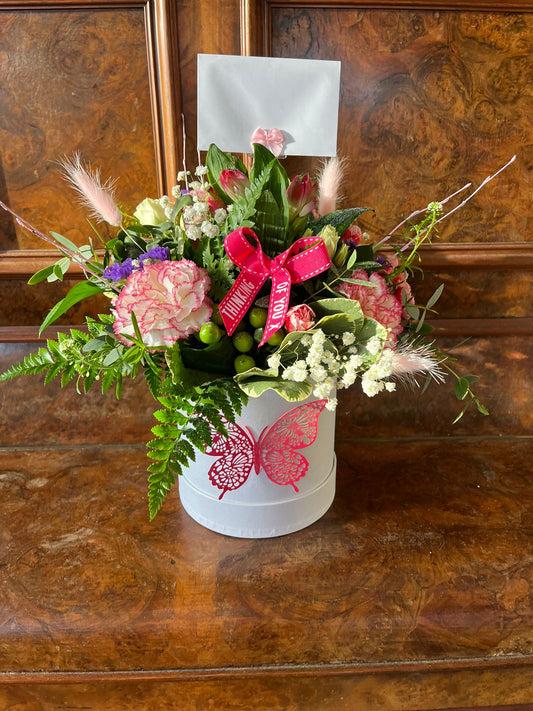 Floral arrangement in a decorative box with a butterfly design on a wooden surface